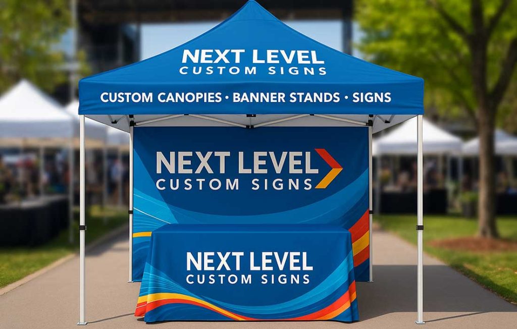 Branded 10 by 10 canopy tent with Next Level Custom Signs logo at outdoor trade show surrounded by trees and event booths